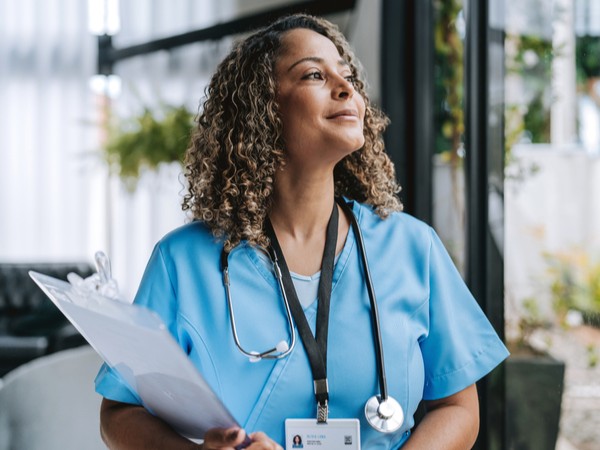 female nurse holding a clipboard looking out a window 
