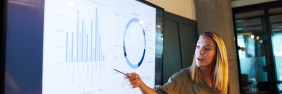 Young blonde businesswoman presenting financial results via a TV screen during a meeting.
