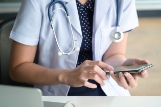 Female nurse with stethoscope around neck using her smartphone to look up medical information.