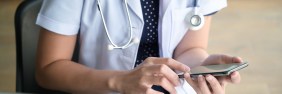Female nurse with stethoscope around neck using her smartphone to look up medical information.