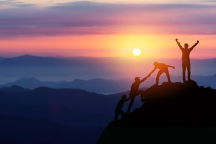 Group of friends climb mountain at sunrise while one friend celebrates at the top.