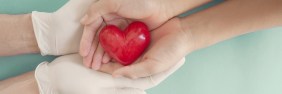 A pair of latex gloved hands holding bare hands that hold a red heart