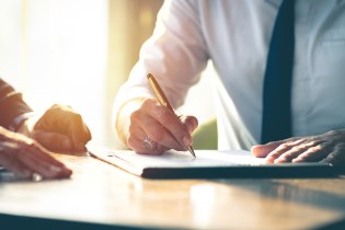 Two men in a business meeting with one man taking notes.