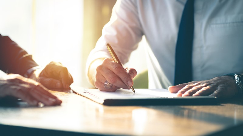 Two men in a business meeting with one man taking notes.