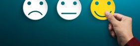 Series of three paper faces, starting with an unhappy face, a neutral face, and a person's hand holding a yellow smiley face.