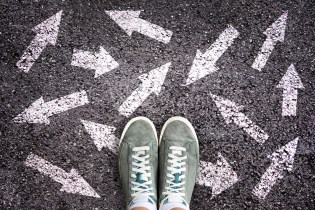 Sneaker shoes and arrows pointing in different directions on asphalt ground, choice concept