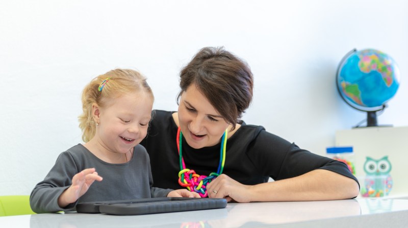 Female toddler in occupational therapy session doing playful exercises on a digital tablet with her occupational therapist.
