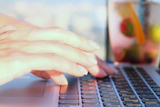 Woman's hands typing on a keyboard outdoors.