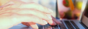 Woman's hands typing on a keyboard outdoors.