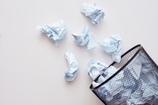 Aerial view of a wire waste basket that tipped over and spilled pieces of crumpled up paper.