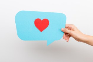 Hand holding a blue speech bubble with a red heart inside