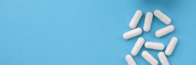 White medication bottle spills 12 white capsules on a light blue background.