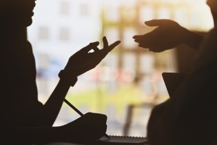 Silhouette of two people chatting and networking while one of them writes things down.