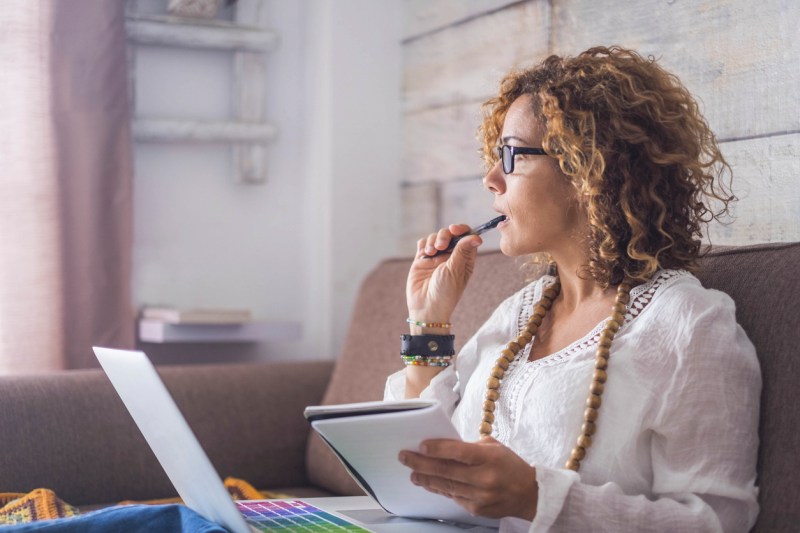 Woman with pen in her mouth ponders over a notebook
