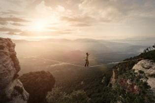 Man walking tightrope across ravine at dawn