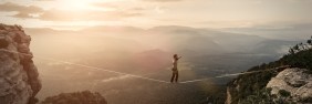 Man walking tightrope across ravine at dawn