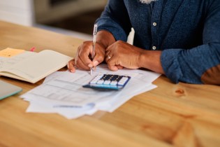 African-American man wearing a blue shirt and calculating commissions for his real estate team.