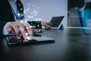 Male real estate broker typing on two different tablets with social media icons floating in the air with numbers of likes and emails.