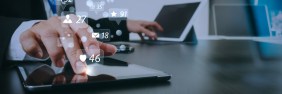 Male real estate broker typing on two different tablets with social media icons floating in the air with numbers of likes and emails.