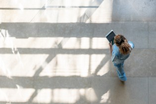 Aerial view of a nurse in blue scrubs entering patient data on a tablet.