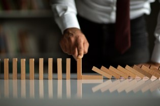 Male business owner with finger on standing domino next to fallen dominoes.