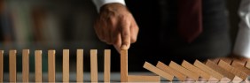 Male business owner with finger on standing domino next to fallen dominoes.