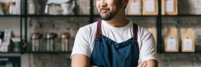 man in an apron and hat with arms folded in front of cafe wall asking himself, "How much general liability insurance coverage do I need"