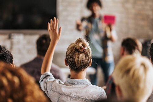 Back view of a young blonde woman raising her hand in the middle of a crowded seminar about errors and omissions insurance