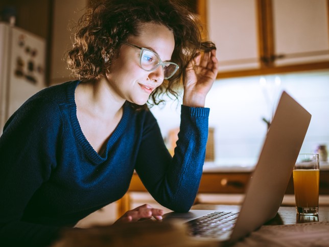 woman smiling at her laptop in a dark room writing about the differences between general liability insurance and professional liability insurance