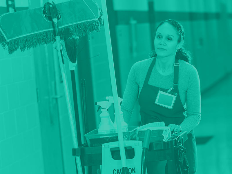woman pushing janitorial cleaning barrel through a hallway 