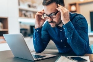 man looking tense, staring at laptop after discovering a mistake he made as a small business owner, preparing to contact his errors and omissions insurance