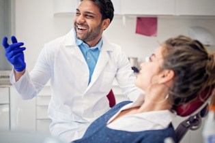 smiling male dentist with female patient in dental chair | How to succeed in owning a dental practice