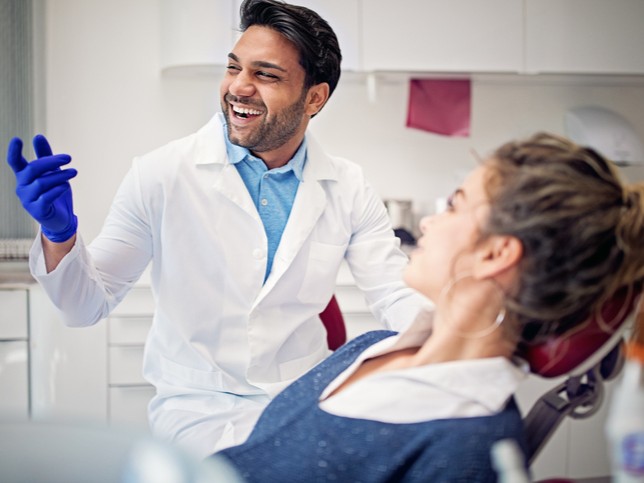 smiling male dentist with female patient in dental chair | How to succeed in owning a dental practice