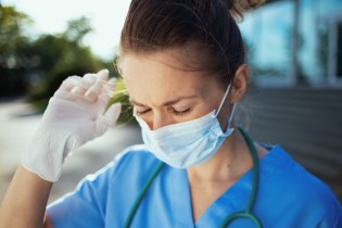 female nurse in mask holding her hand to her head looking stressed | rn licensing board complaint