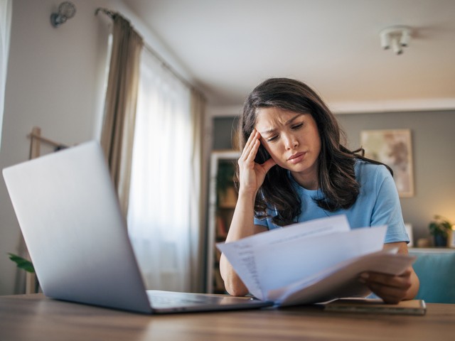 stressed woman reading papers while on her laptop 
