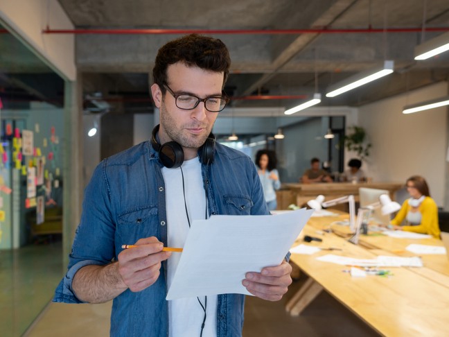 Creative man with headphones and a pencil and paper reviewing his errors and omissions insurance policy