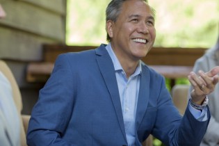 Smiling man in suit sitting with others and smiling | Who Needs Errors and Omissions Liability Insurance?