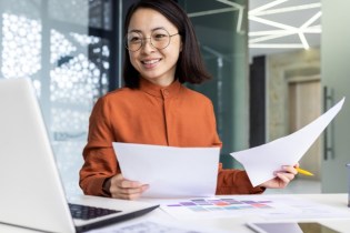 Woman in orange holding papers at her desk while smiling | Errors and Omissions Insurance Costs