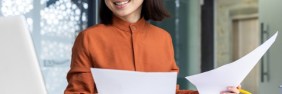 Woman in orange holding papers at her desk while smiling | Errors and Omissions Insurance Costs