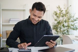 smiling business owner calculating | small business insurance cost on calculator | How Much Does $1 Million General Liability Insurance Cost?