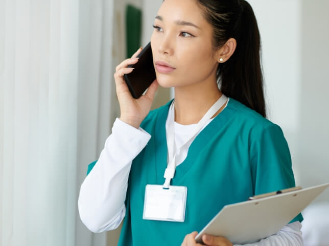 nurse holding a clipboard and talking on the phone with her insurance company 