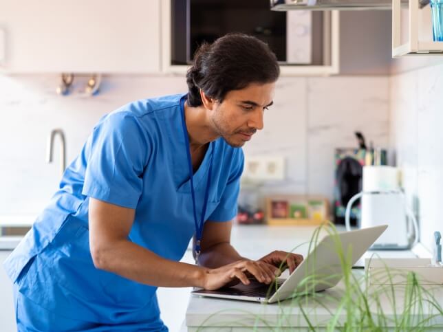 Male nurse on laptop in kitchen looking up how to get insurance