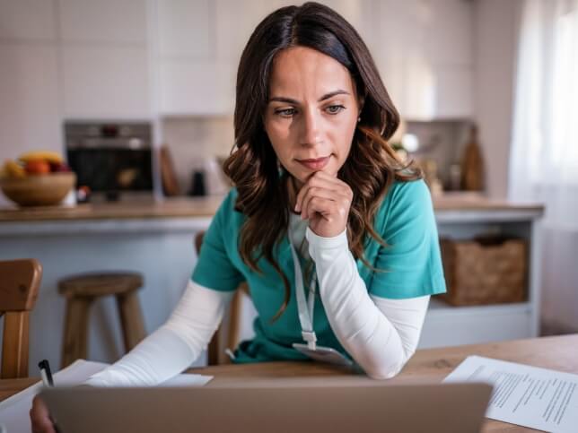 Female nurse sitting at kitchen table with laptop comparing insurance coverages 