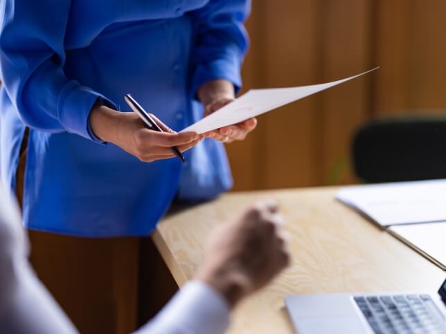 Woman in blue shirt holding pen and reviewing documents 