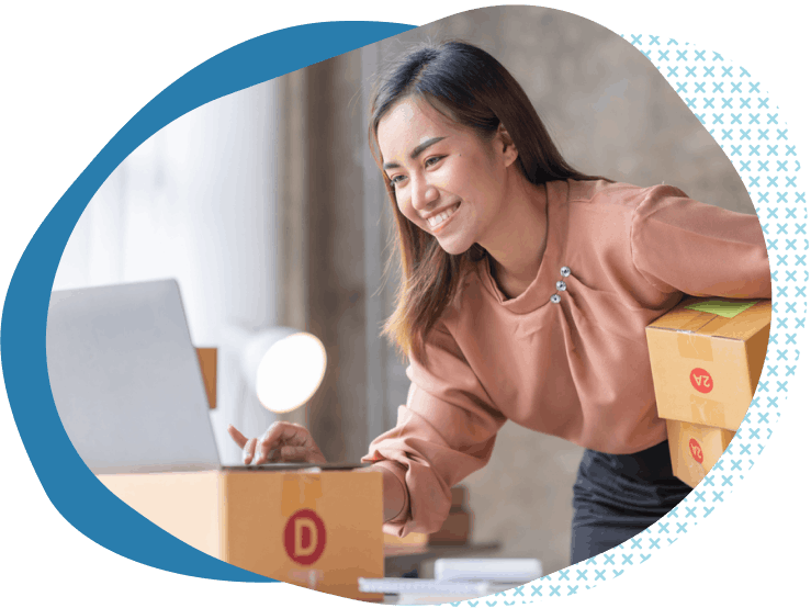 female business owner holding boxes while researching liability insurance for ecommerce on her computer
